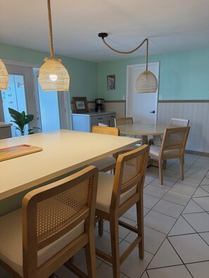 Uma sala de jantar com mesa, cadeiras, cafeteira e luminária pendente.