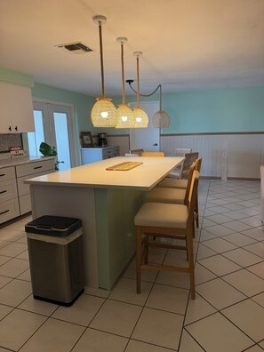 A kitchen with a central island, hanging pendant lights, a trash bin, and a dining area with chairs. - Welcoming 3-bedroom house on canal with direct gulf access (Hernando Beach)