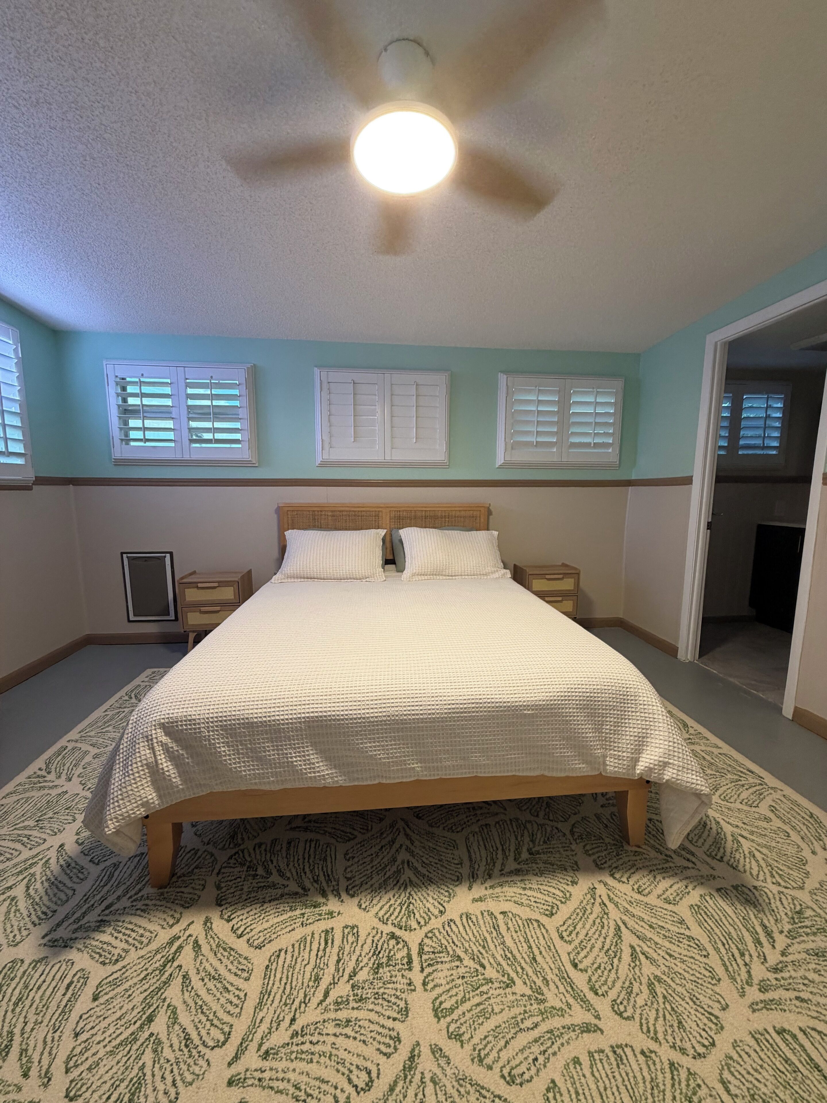 Une chambre à coucher avec un lit, deux tables de chevet, un ventilateur de plafond et un tapis à motifs.