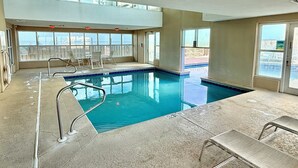Uma piscina interior com paredes de vidro transparente, uma cadeira de salva-vidas e uma escada de piscina.