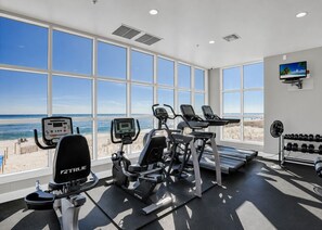 Ein Fitnessraum mit Cardiogeräten, einem Fernseher und Blick auf den Strand.
