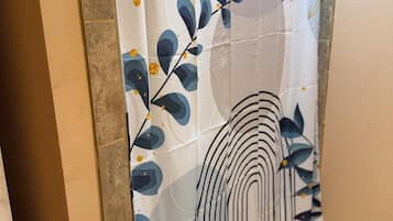 A bathroom with a shower curtain featuring a leaf and wave pattern, a tiled floor, and a showerhead.