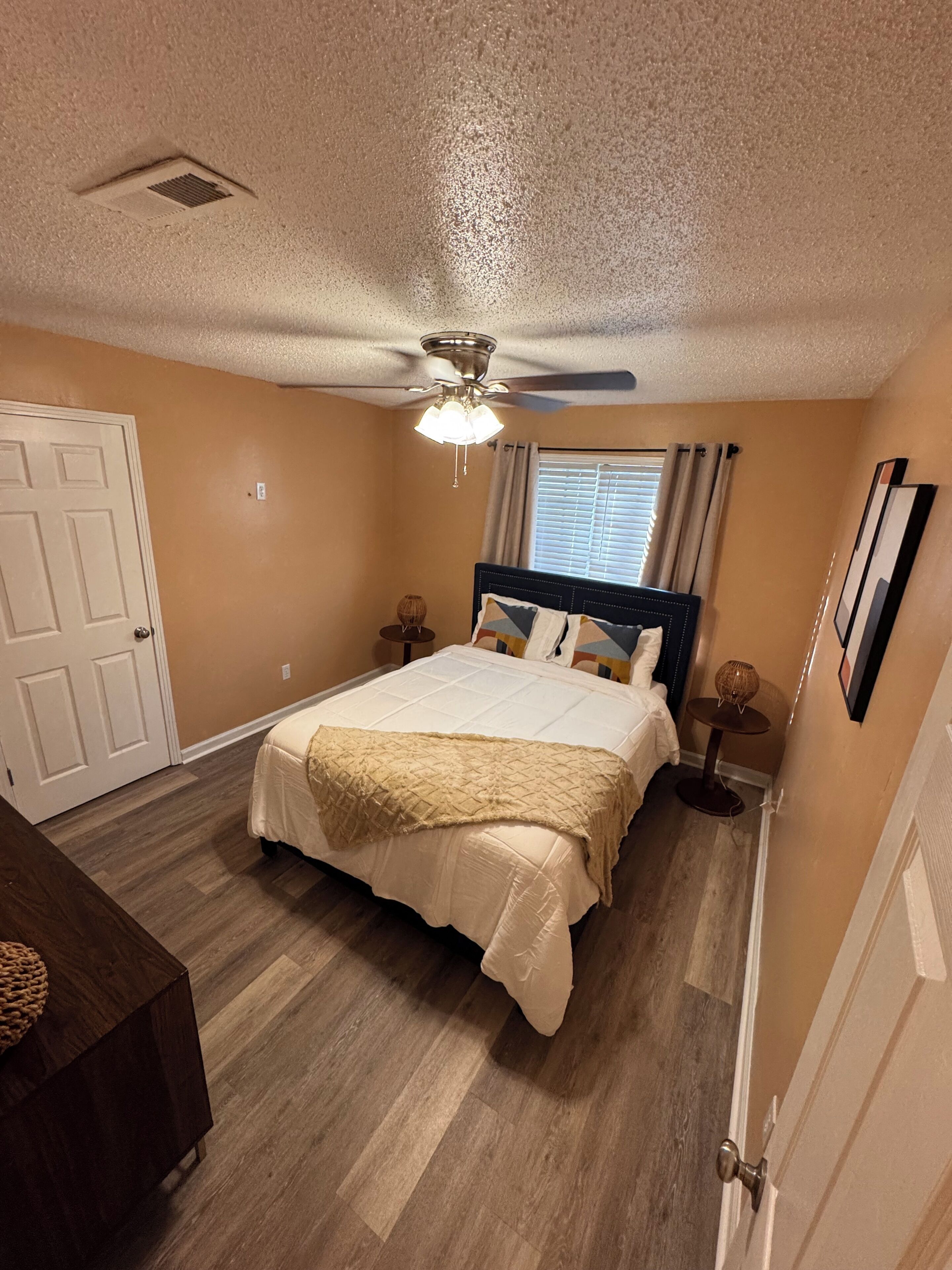 A bedroom with a bed, a ceiling fan, a window with curtains, a bedside table, and a nightstand.