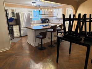 A kitchen with a central island, bar stools, a refrigerator, and a dining table. - Where Delta History Meets Modern Luxury (Mound Bayou)