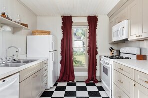 A kitchen with white cabinets, a black and white checkered floor, a refrigerator, a microwave, a stove, and a sink. - Northern Sky Cottages | 3 Houses | 8BR | 4BA | 2 Hot Tubs | Game Shed & Private Yard (Traverse City)
