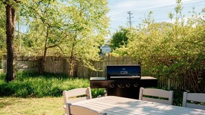 Patio esterno con barbecue, tavolo e sedie.