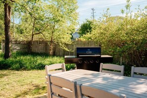 An outdoor patio with a barbecue grill, a table, and chairs. - Northern Sky Cottages | 3 Houses | 8BR | 4BA | 2 Hot Tubs | Game Shed & Private Yard (Traverse City)