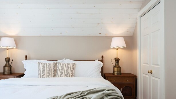 Una camera da letto con un letto, due lampade da comodino, un comodino in legno e una porta bianca.