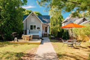 A house with a porch, a grill, and a table with chairs.