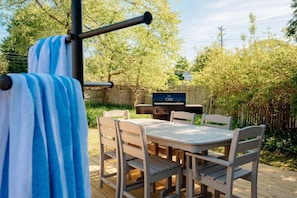 Un espacio exterior para comer con una mesa y sillas de madera, una parrilla y una terraza de madera.