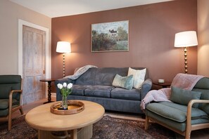 A living room with a sofa, two armchairs, a coffee table with a vase of flowers, and two floor lamps. - Northern Sky Cottages | 3 Houses | 8BR | 4BA | 2 Hot Tubs | Game Shed & Private Yard (Traverse City)
