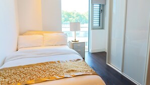 Ein Schlafzimmer mit einem Bett, einem Nachttisch, einer Lampe und Blick ins Freie durch ein Fenster.