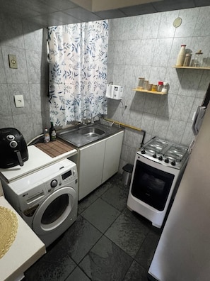 A compact kitchen with a washing machine, a stove, and a sink. - Studio Copanema (Rio de Janeiro)