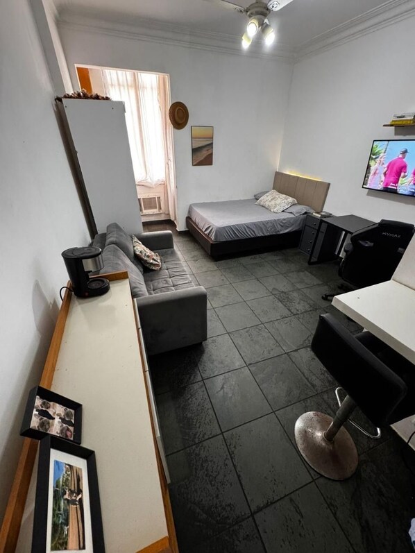 A compact room with a bed, a desk, a chair, a television, and a small kitchenette area. - Studio Copanema (Rio de Janeiro)