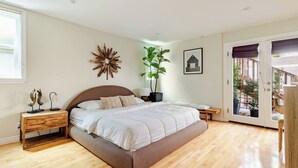 Ein Schlafzimmer mit Bett, Nachttischen, einem großen Fenster, einer zur Außenseite führenden Tür und einer Wanddekoration.