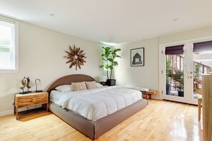 Ein Schlafzimmer mit Bett, Nachttischen, einem großen Fenster, einer zur Außenseite führenden Tür und einer Wanddekoration.
