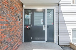 A black door with a keypad and a card reader, a window with a security camera, and a brick wall. - Elegant Living in a 1-Bedroom Suite (Edmonton)