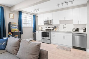 Una cocina moderna con armarios blancos, electrodomésticos de acero inoxidable y una zona de comedor con sofá gris.