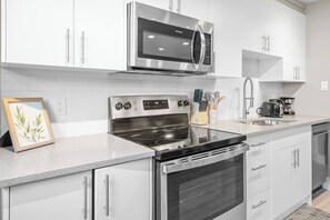 A modern kitchen with stainless steel appliances, white cabinetry, and a granite countertop. - Elegant Living in a 1-Bedroom Suite (Edmonton)