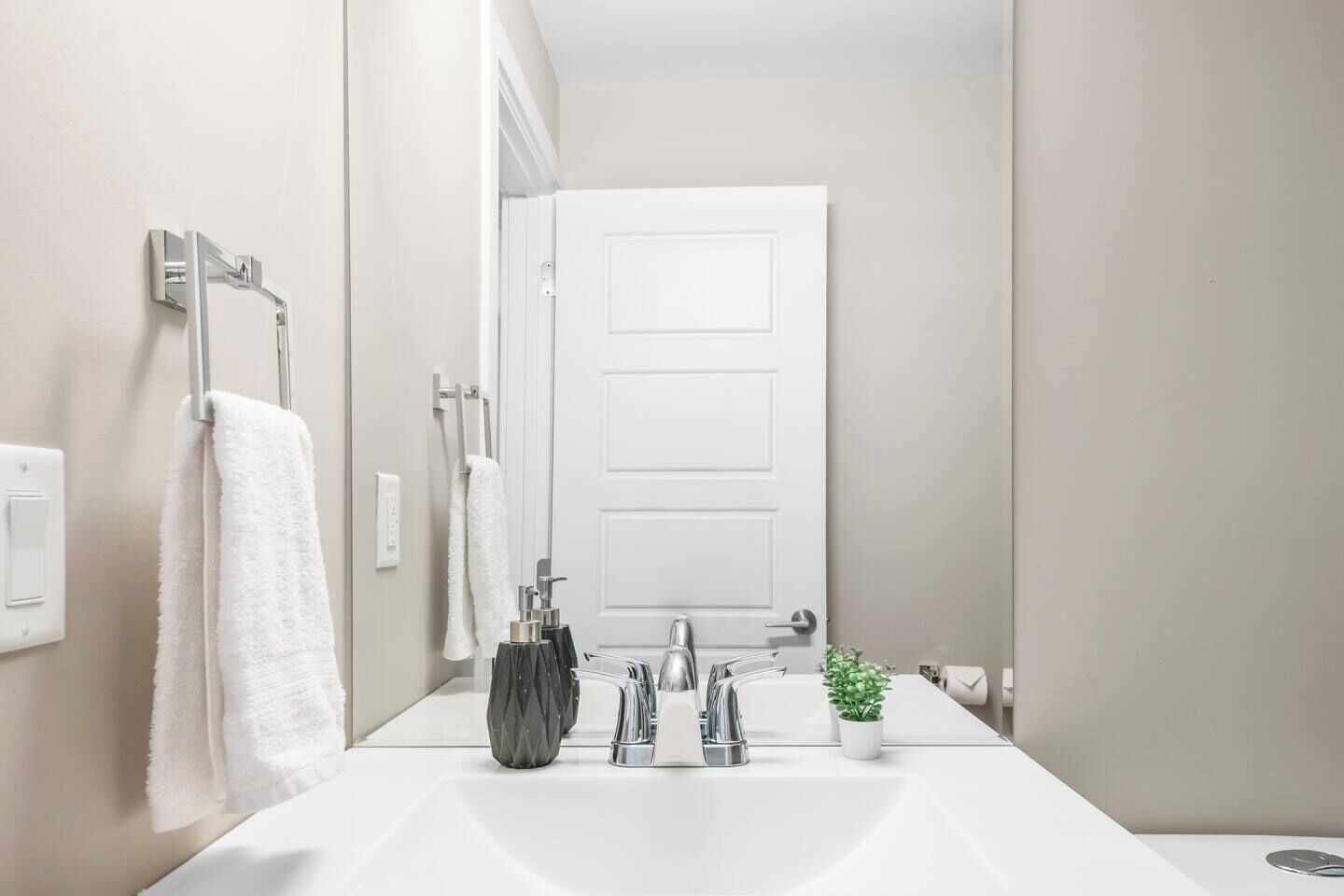 A modern bathroom with a white sink, chrome faucet, and a potted plant.