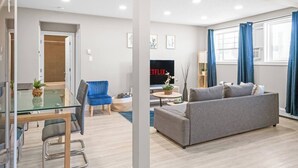 A modern living room with a grey sofa, a blue chair, a glass table, and a TV displaying 'NETFLIX'. - Elegant Living in a 1-Bedroom Suite (Edmonton)