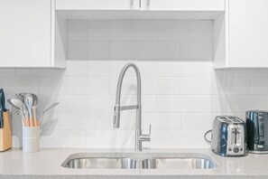 A kitchen with a stainless steel sink, a modern faucet, and two toasters on the counter. - Elegant Living in a 1-Bedroom Suite (Edmonton)