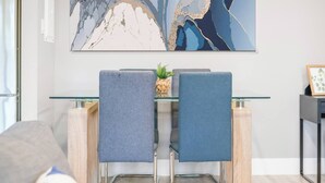 A modern dining area with a glass table and metal chairs, a decorative wall piece, and a small plant on the table. - Elegant Living in a 1-Bedroom Suite (Edmonton)