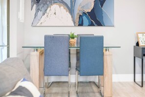 A modern dining area with a glass table and metal chairs, a decorative wall piece, and a small plant on the table. - Elegant Living in a 1-Bedroom Suite (Edmonton)