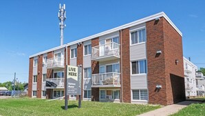 A multi-story apartment building with balconies, a sign advertising available apartments, and a clear blue sky. - Elegant Living in a 1-Bedroom Suite (Edmonton)