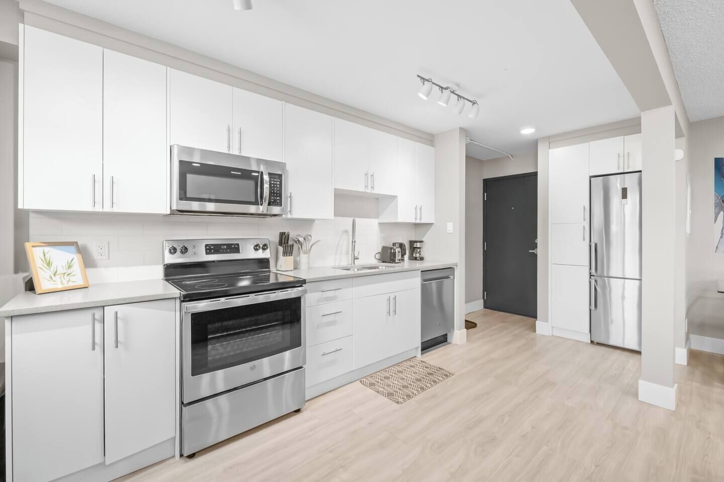 Une cuisine moderne dotée d’appareils électroménagers en acier inoxydable, de meubles blancs et d’un plancher en bois clair.