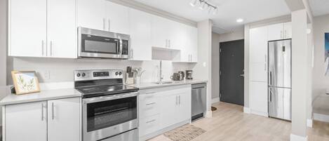 Une cuisine moderne dotée d’appareils électroménagers en acier inoxydable, de meubles blancs et d’un plancher en bois clair.