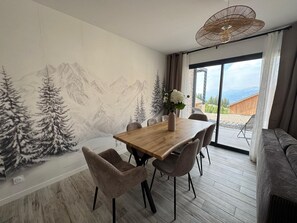 Ein Essbereich mit einem Holztisch, Stühlen, einer Blumenvase und einem Wandgemälde mit einer Berglandschaft.