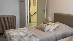 A bedroom with two beds, a wooden bench, a nightstand, and a door leading to another room. - Chalet Altéa - 7 à 8 pers - Neuf & Cosy - 300 m des Pistes (Risoul)