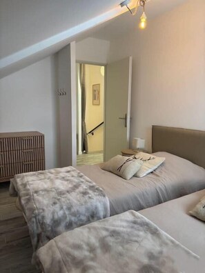 Un dormitorio con dos camas, un banco de madera, una mesita de noche y una puerta que da a otra habitación.