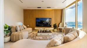 Ein modernes Wohnzimmer mit großem Flachbildfernseher, einer Couch, einem Couchtisch und Blick auf den Ozean.