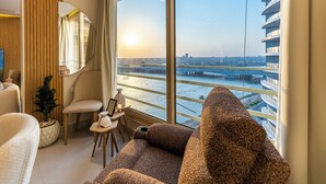 Ein modernes Hotelzimmer mit großem Fenster, einer Couch, einem Sessel, einem kleinen Tisch mit Blumenvase und einer Zimmerpflanze.