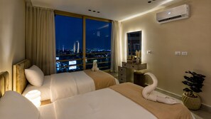 Ein Hotelzimmer mit zwei Betten, einem großen Fenster mit Blick auf die Stadt, einer Klimaanlage und einem Nachttisch mit einer Vase und Büchern.