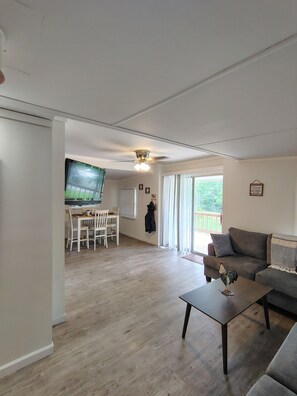 Ein Wohnzimmer mit Fernseher, Essbereich, Deckenventilator und Blick ins Freie.