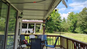 A covered outdoor deck with chairs and a table, overlooking a grassy area with trees. - Near Kentucky lake Running bear cottage ! (Gilbertsville)