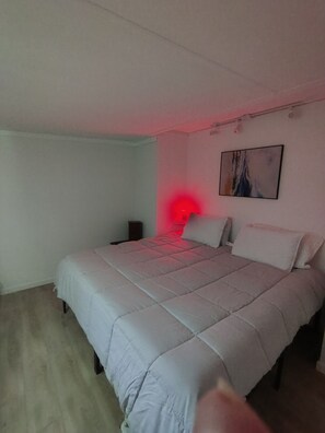 Ein Schlafzimmer mit Bett, Nachttisch, Wandbild und rotem Licht.
