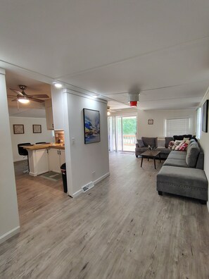 Ein modernes Wohnzimmer mit einem grauen Sofa, einem Essbereich mit einem Holztisch und einer Küche mit weißen Schränken.