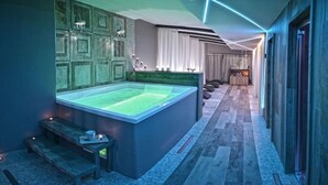 A modern bathroom with a large bathtub, wooden benches, and a vanity with a mirror. - Vea Resort Hotel (Mercato San Severino)