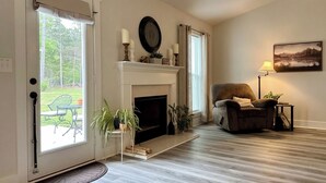 A living room with a fireplace, a chair, a table, and a door leading to a patio. - Brand New Home! Modern Lake Retreat: 1 Mi to Water & Boat Parking (Hartwell)