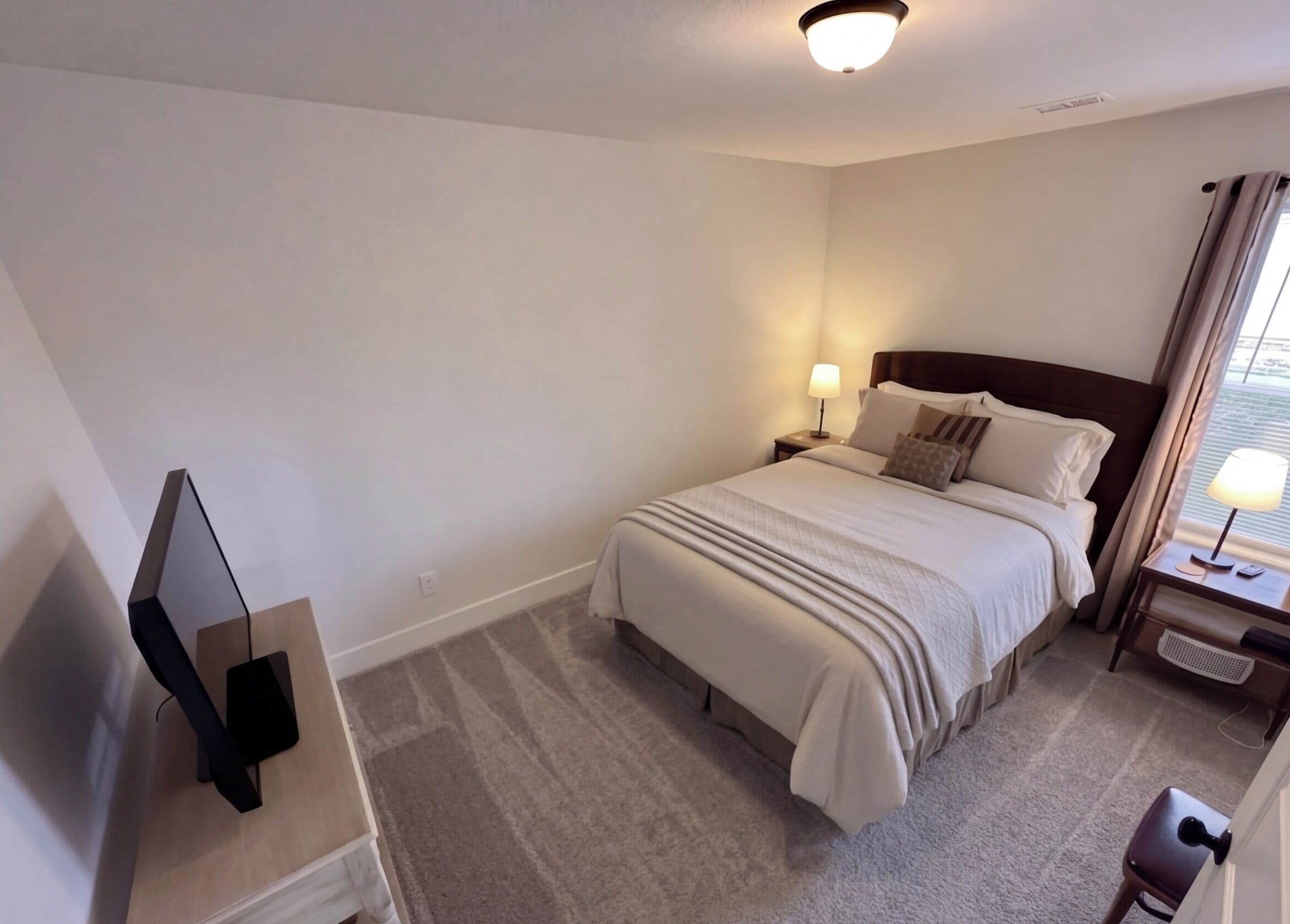 Una habitación de hotel con cama, mesita de noche con lámpara, televisión y una silla.
