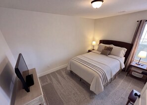 A hotel room with a bed, a bedside table with a lamp, a TV, and a chair. - Brand New Home! Modern Lake Retreat: 1 Mi to Water & Boat Parking (Hartwell)