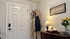 A hallway with a white door, coat hooks with coats, a lamp, a book, and a vase with flowers. - Brand New Home! Modern Lake Retreat: 1 Mi to Water & Boat Parking (Hartwell)