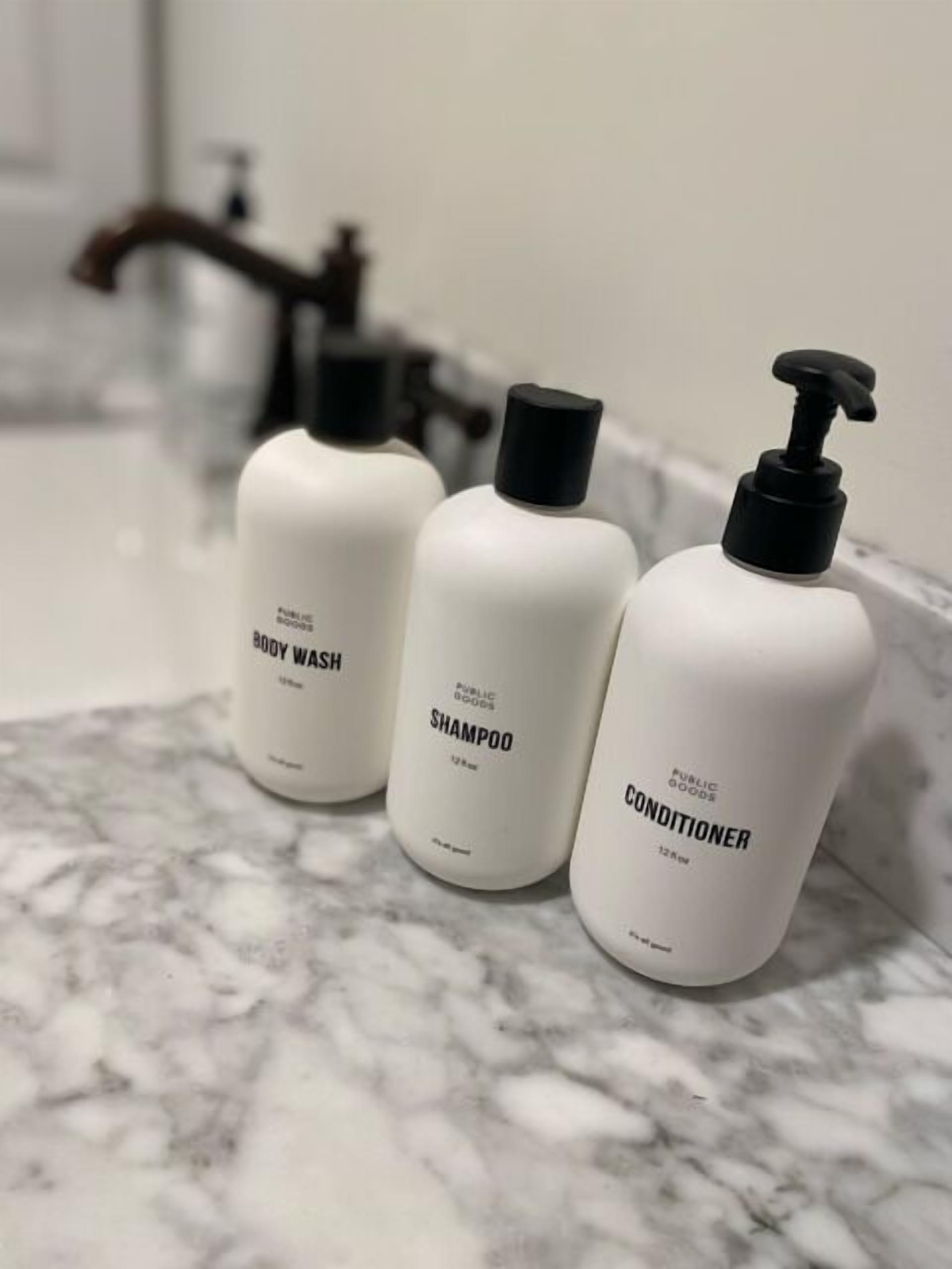 Three bottles of body wash, shampoo, and conditioner on a marble countertop.