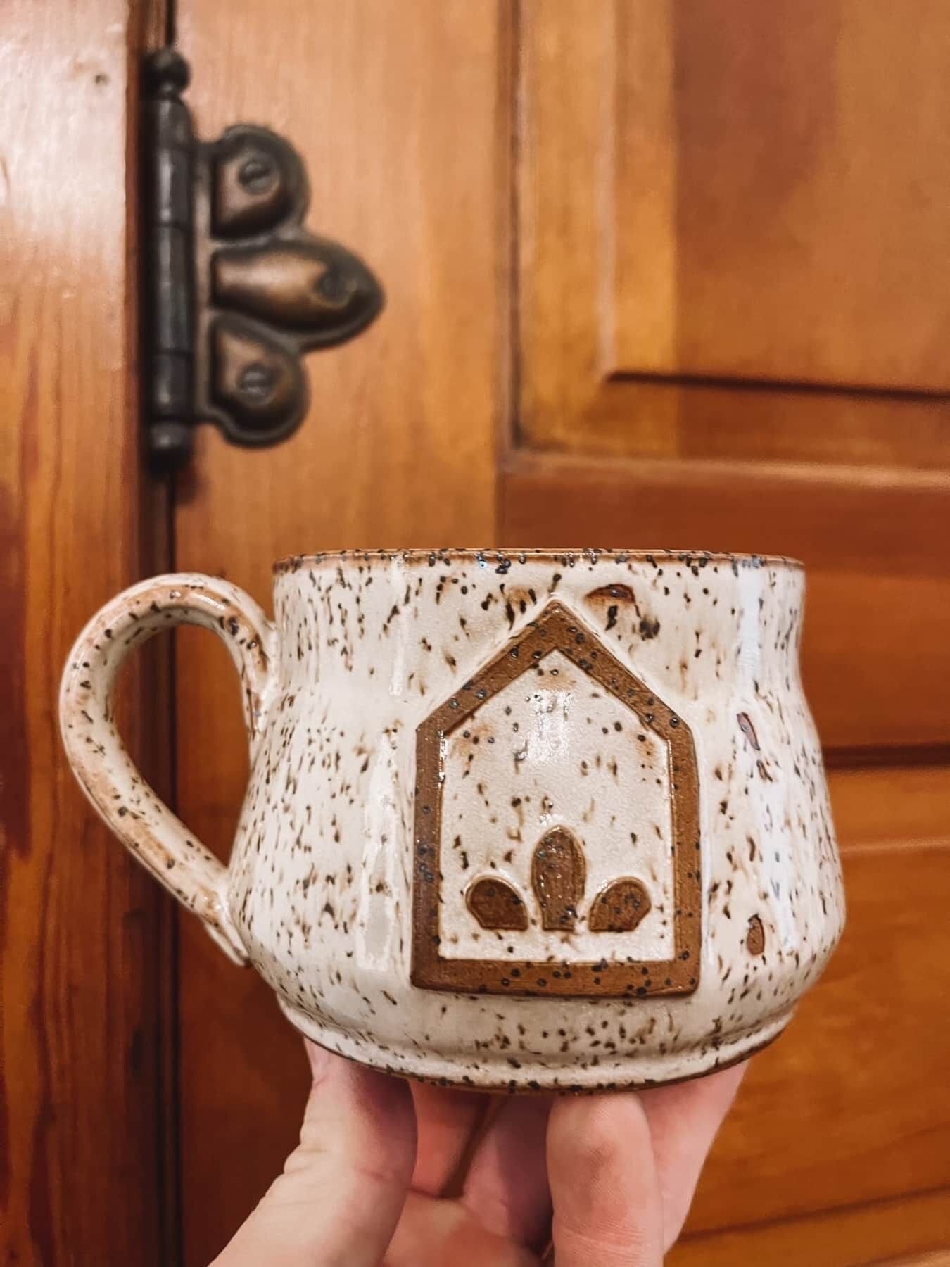 Een hand die een keramische mok vasthoudt, versierd met een ontwerp van een huis.