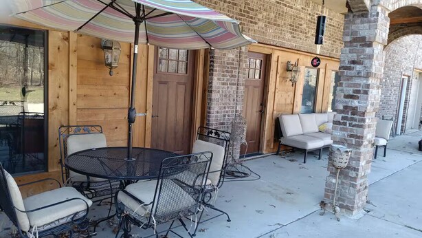 Een buitenpatio met een ronde tafel en stoelen, een gestreepte parasol en bakstenen muren.