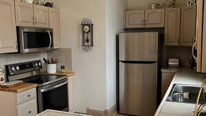 Een keuken met een magnetron, fornuis, koelkast en een klok aan de muur.